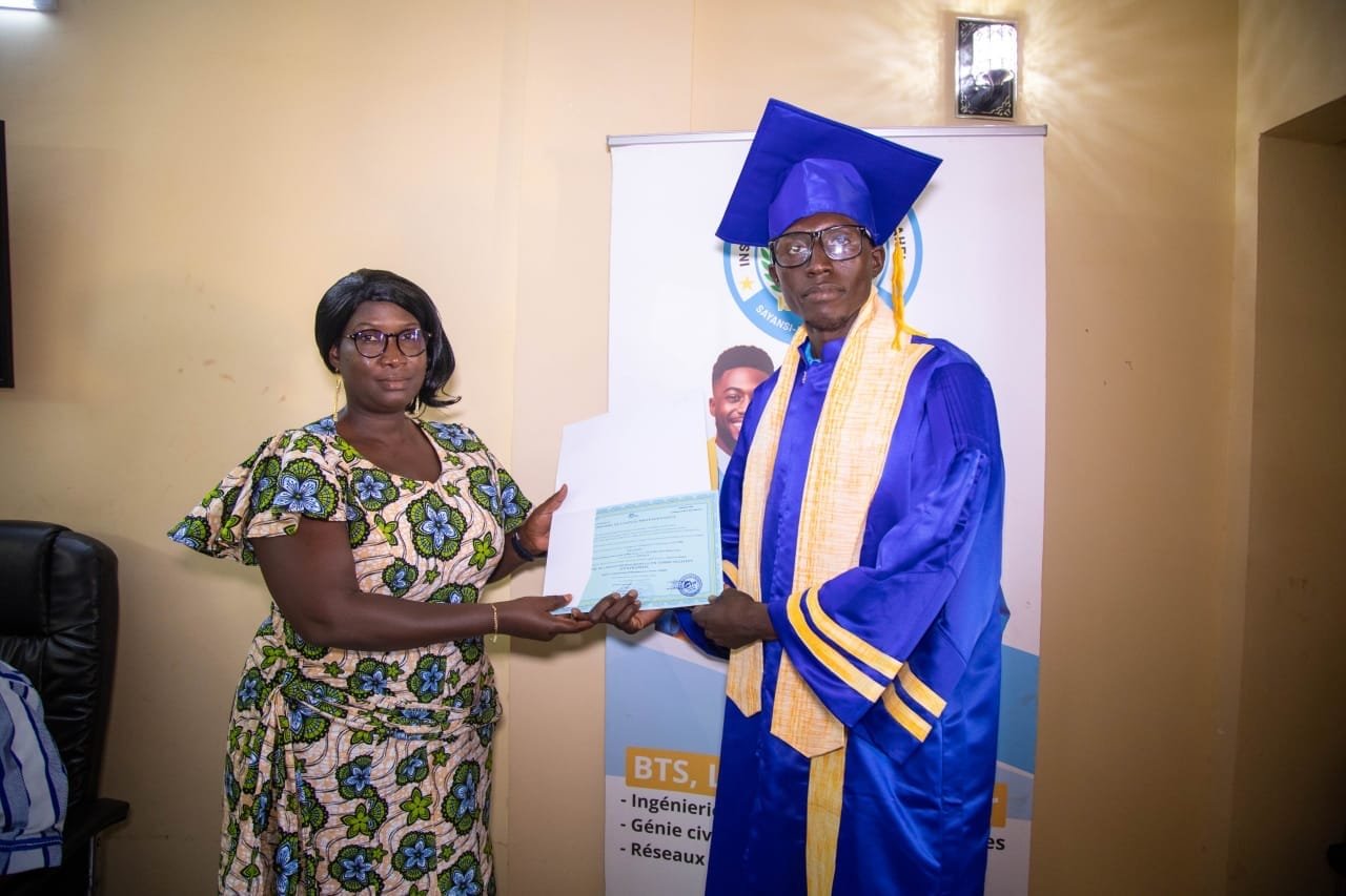 Une représentante de l'institut remet son diplôme à un diplômé en toge bleue, devant une bannière de l'ISP SAHEL