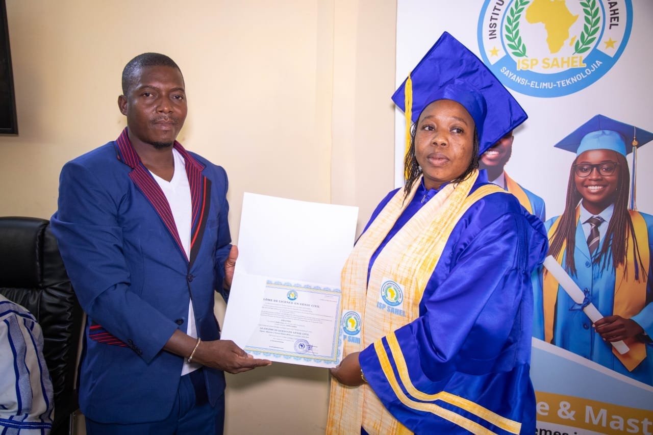 Une diplômée en toge bleue reçoit son diplôme de Licence en Génie civil devant la bannière de l'ISP SAHEL