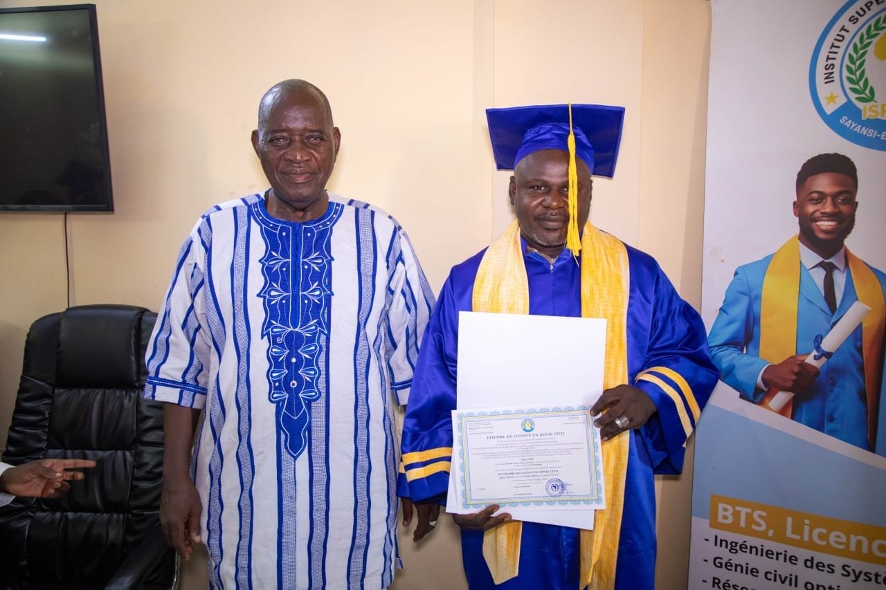 Un diplômé en toge bleue présente son diplôme de Licence en Génie civil aux côtés d'un aîné en boubou, devant une bannière de l'ISP SAHEL