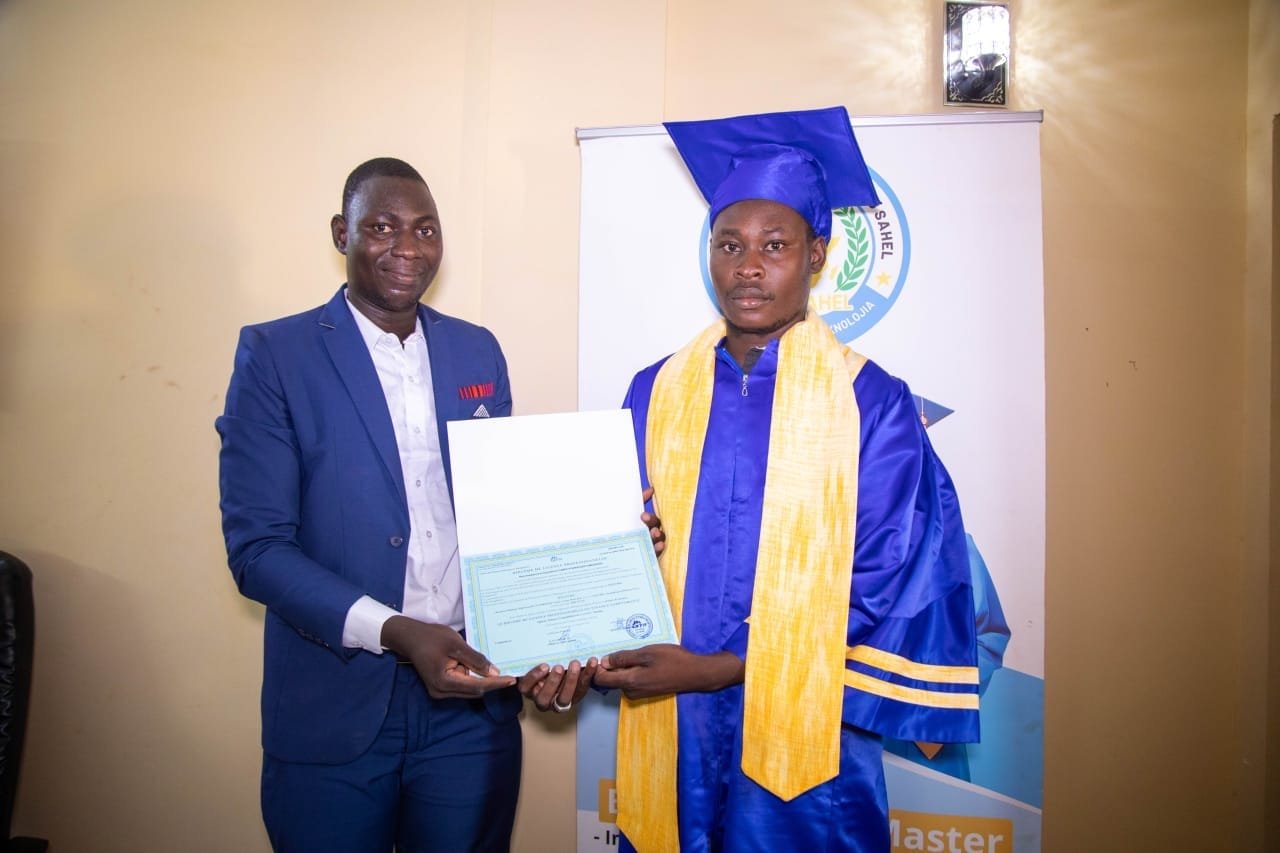 Un représentant de l'institut en costume remet son diplôme à un jeune diplômé devant la bannière de l'ISP SAHEL