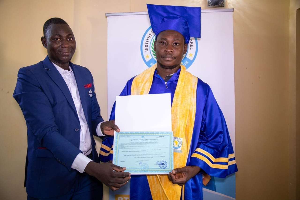 Un diplômé présente son diplôme de Licence professionnelle aux côtés d'un représentant de l'institut en costume