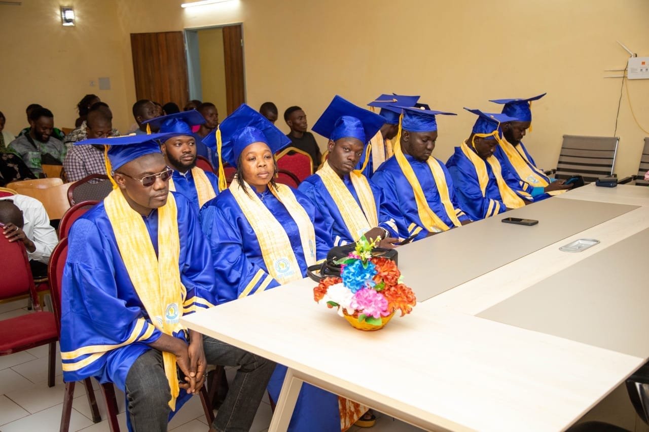 Une rangée de diplômés en toge bleue et étole jaune assis autour d'une table décorée de fleurs