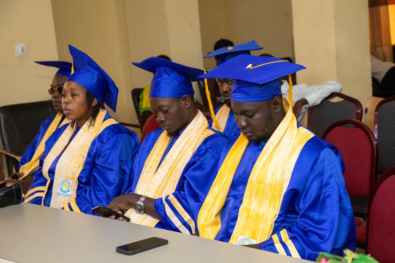 Une rangée de diplômés en toge bleue et étole jaune assis à une table pendant la cérémonie