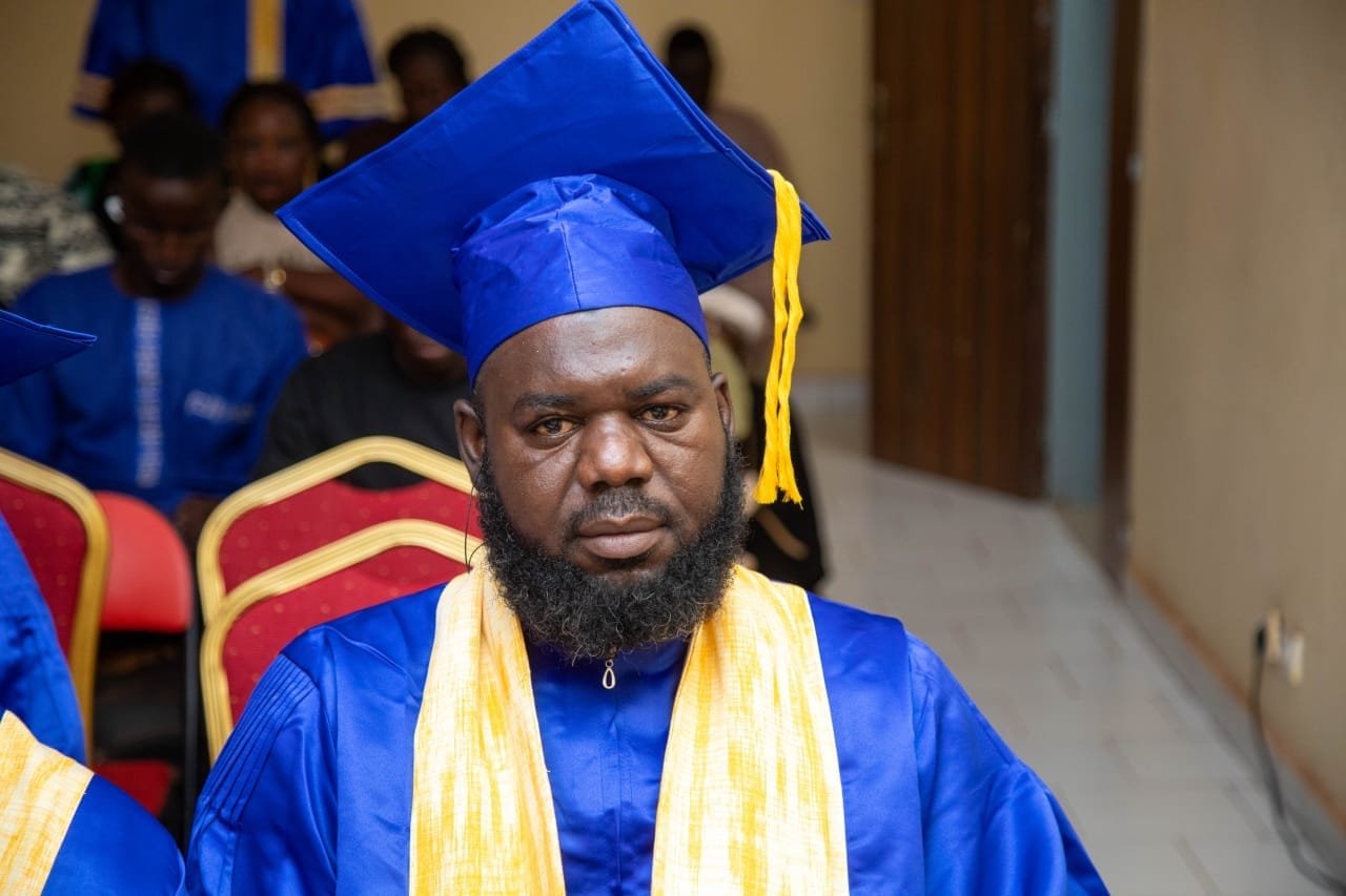 Un diplômé barbu en toge bleue et étole jaune assis pendant la cérémonie