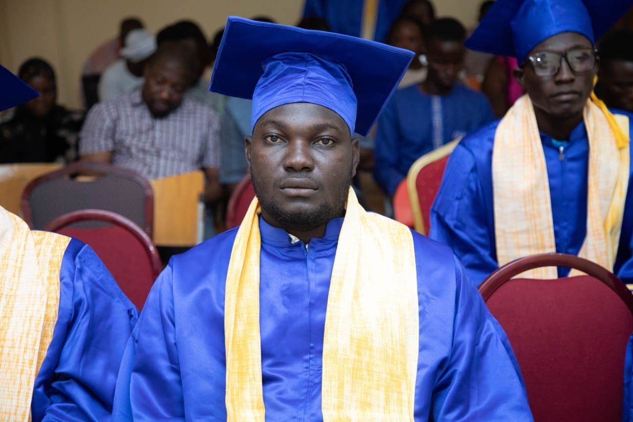 Un diplômé en toge bleue et étole jaune assis au premier rang