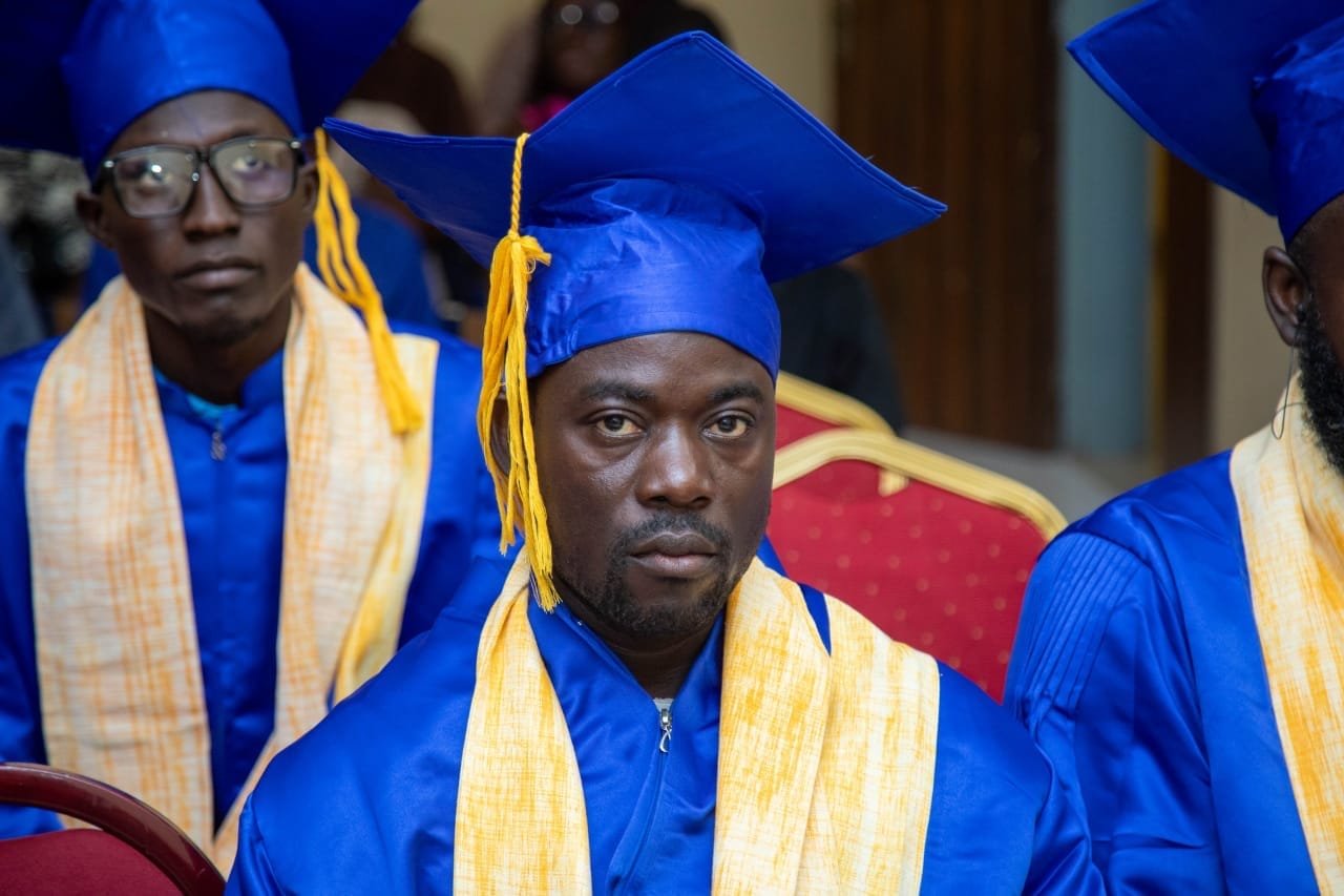 Un diplômé en toge bleue et étole jaune, d'autres diplômés derrière lui