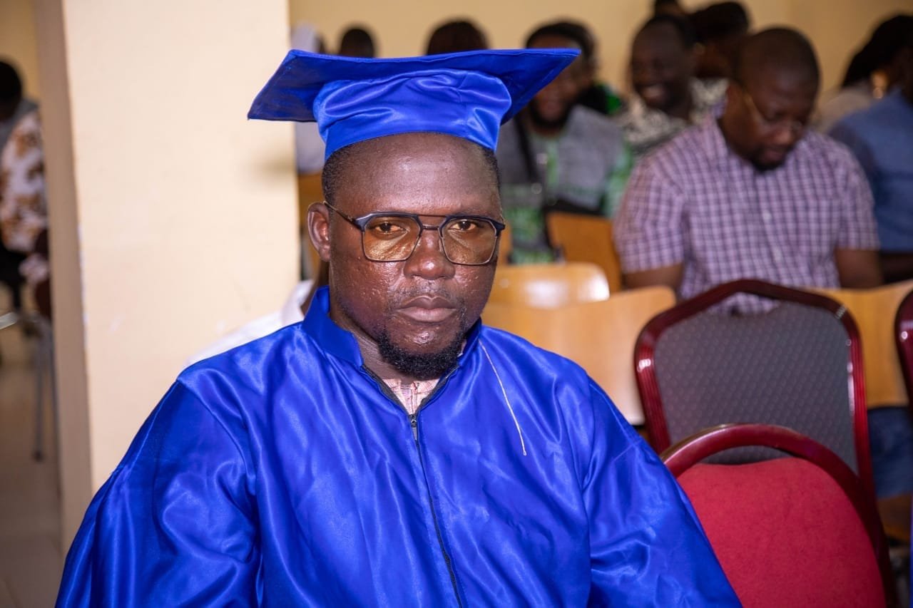 Un diplômé à lunettes en toge bleue assis dans la salle de cérémonie
