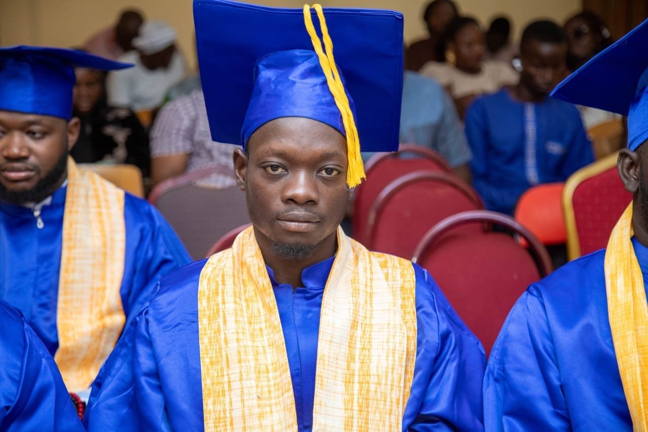 Un jeune diplômé en toge bleue et étole jaune assis au premier rang